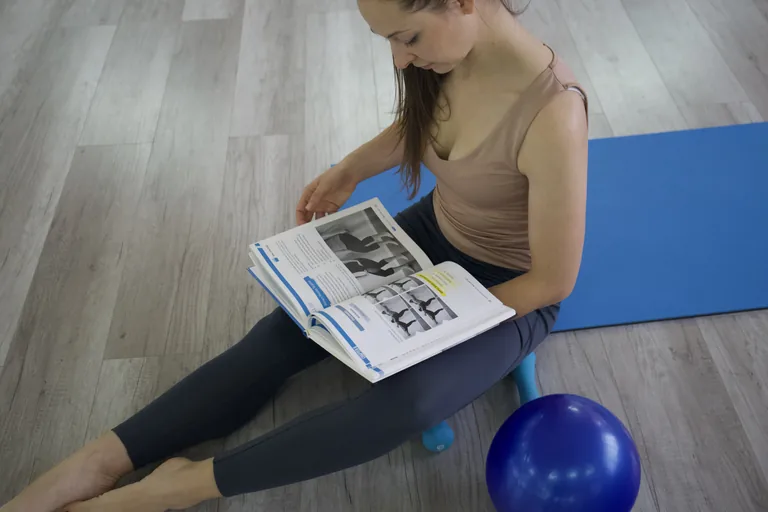 A participant reads an illustrated workbook beside a blue exercise mat.