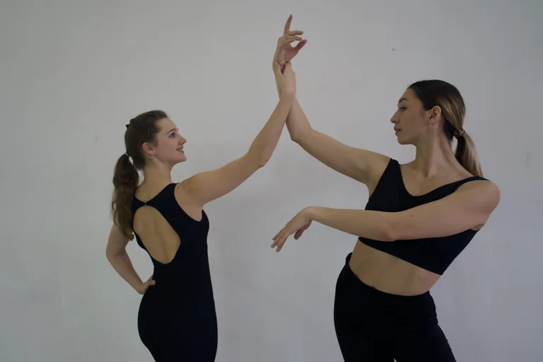 Two participants demonstrate arm positioning together in a studio.