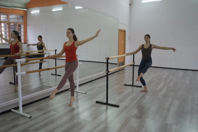Two participants practise standing barre positions in a mirrored studio.
